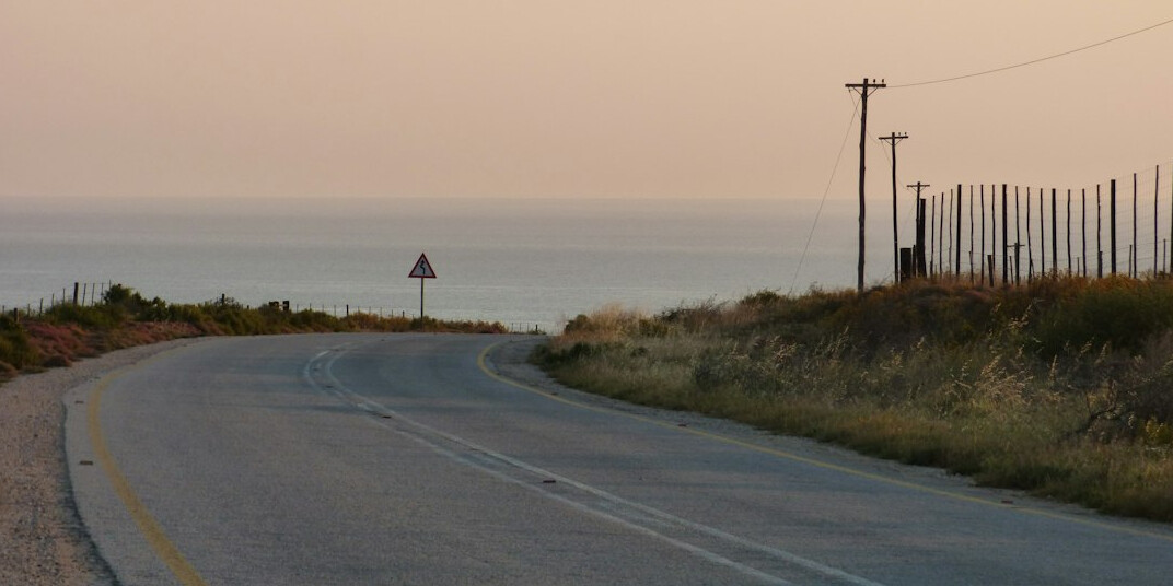 Sports car driving on a coastal road at sunset